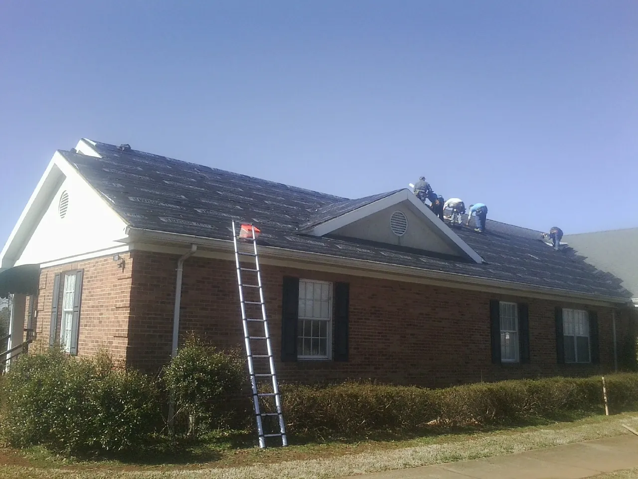 Crew tearing shingles off a brick ranch roof with a ladder set — Emergency Roof Repair work by our crew in Lily