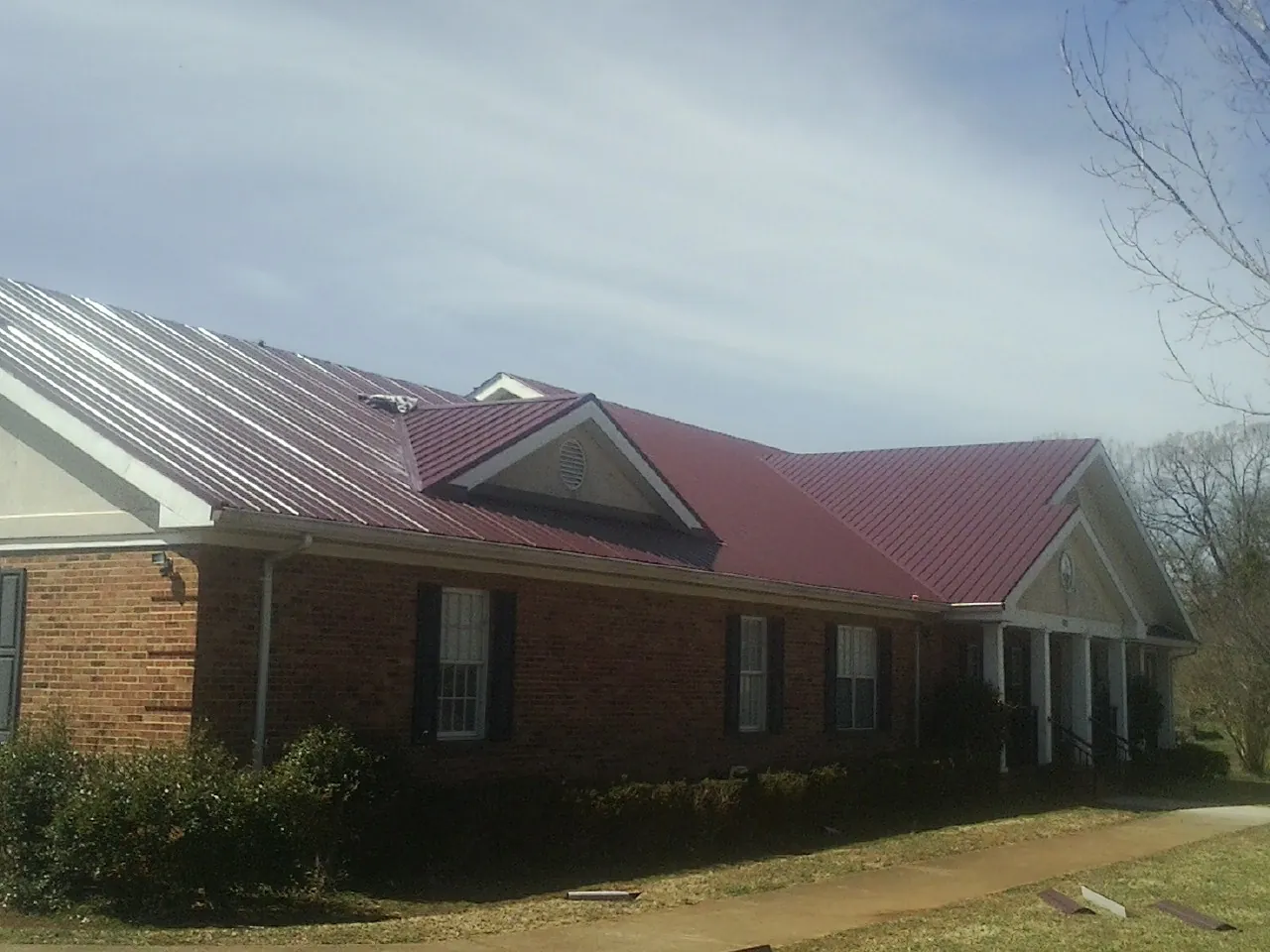 Red metal roof with gabled entries on a long brick building, from a Hail Damage Roof Repair job in Lily