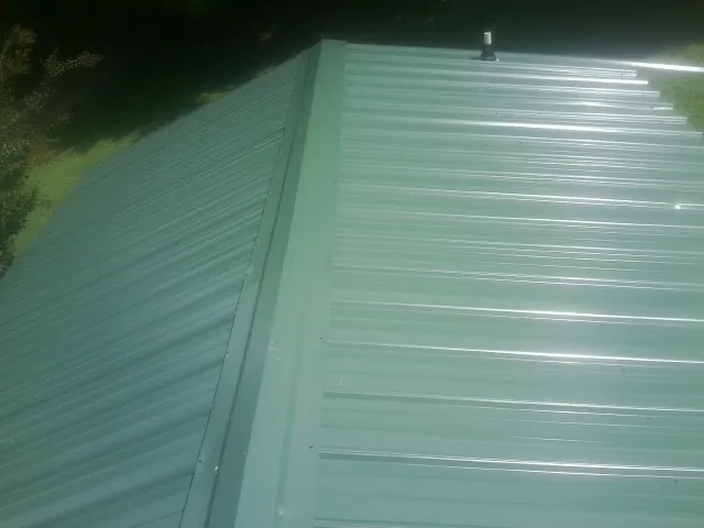 New green metal panels meeting at the ridge of a roof — Flat Roof Repair work by our crew in Lily