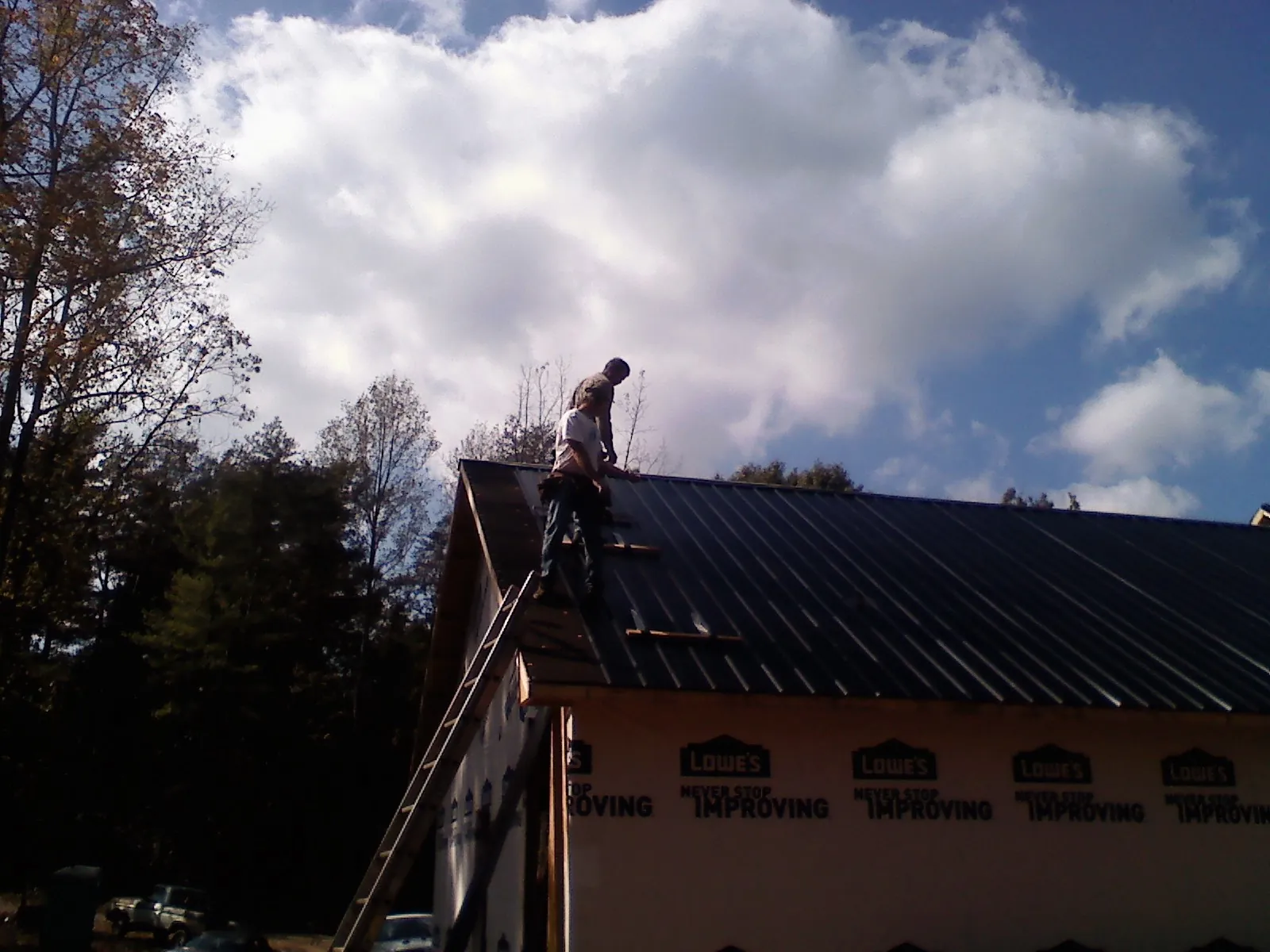 Roofer fastening dark metal panels high against a cloudy sky, from a Roof Inspection job in Lily