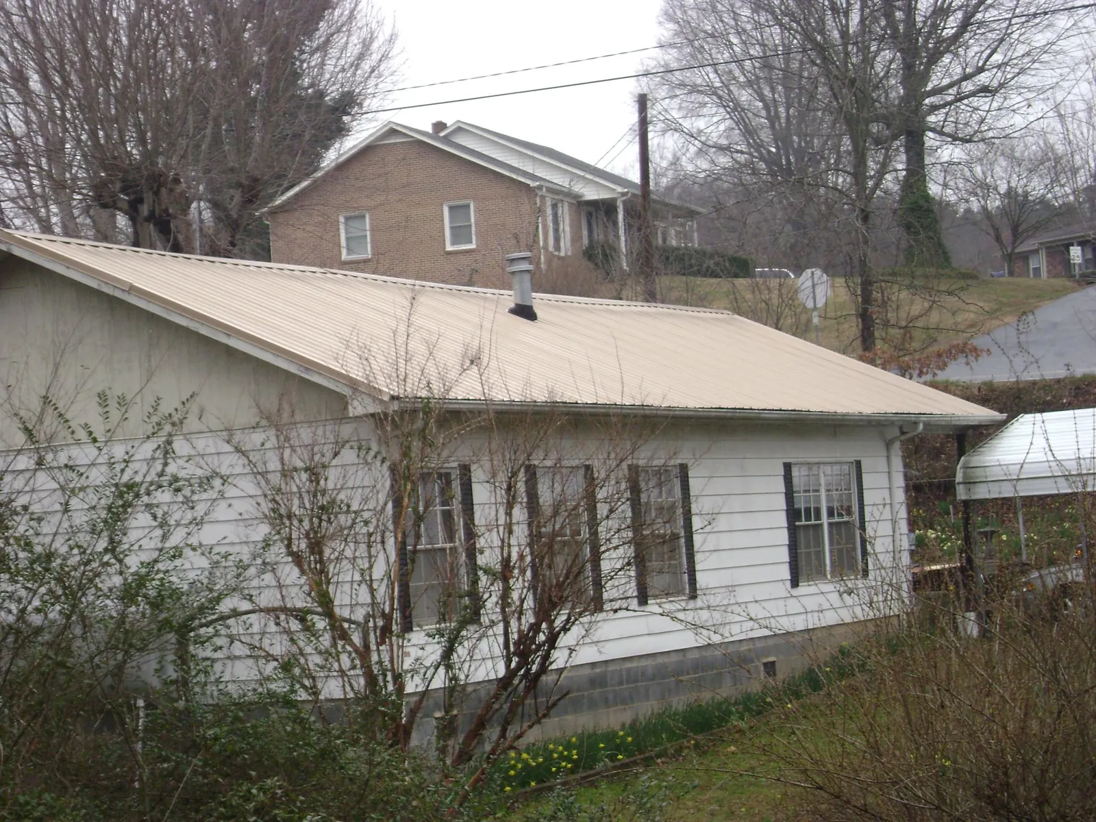Tan metal roof on a white sided house set into a hillside — Commercial Roofing by Roofing Brothers in Lily